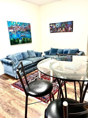 A living room with a blue sofa, a glass coffee table, and two paintings on the wall. - Modern & Cozy Stay | Self Check-In | Free Parking (Surrey)