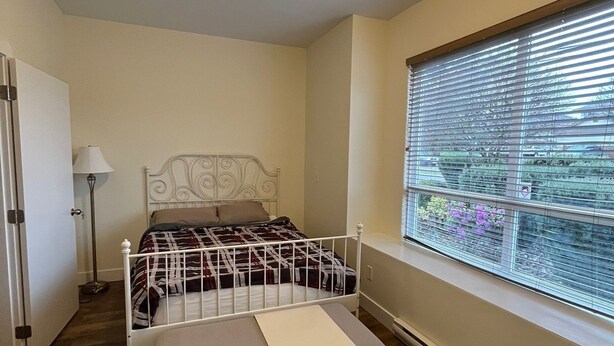 A bedroom with a bed, a bedside table, a lamp, a window with blinds, and a radiator. - Modern & Cozy Stay | Self Check-In | Free Parking (Surrey)