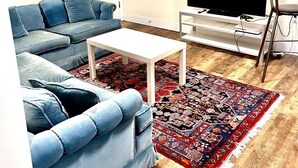 A living room with a blue sofa, a white coffee table, a flat-screen TV, and a patterned rug. - Modern & Cozy Stay | Self Check-In | Free Parking (Surrey)