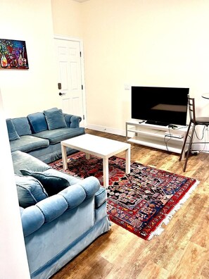 A living room with a blue sofa, a white coffee table, a flat-screen TV, and a patterned rug. - Modern & Cozy Stay | Self Check-In | Free Parking (Surrey)