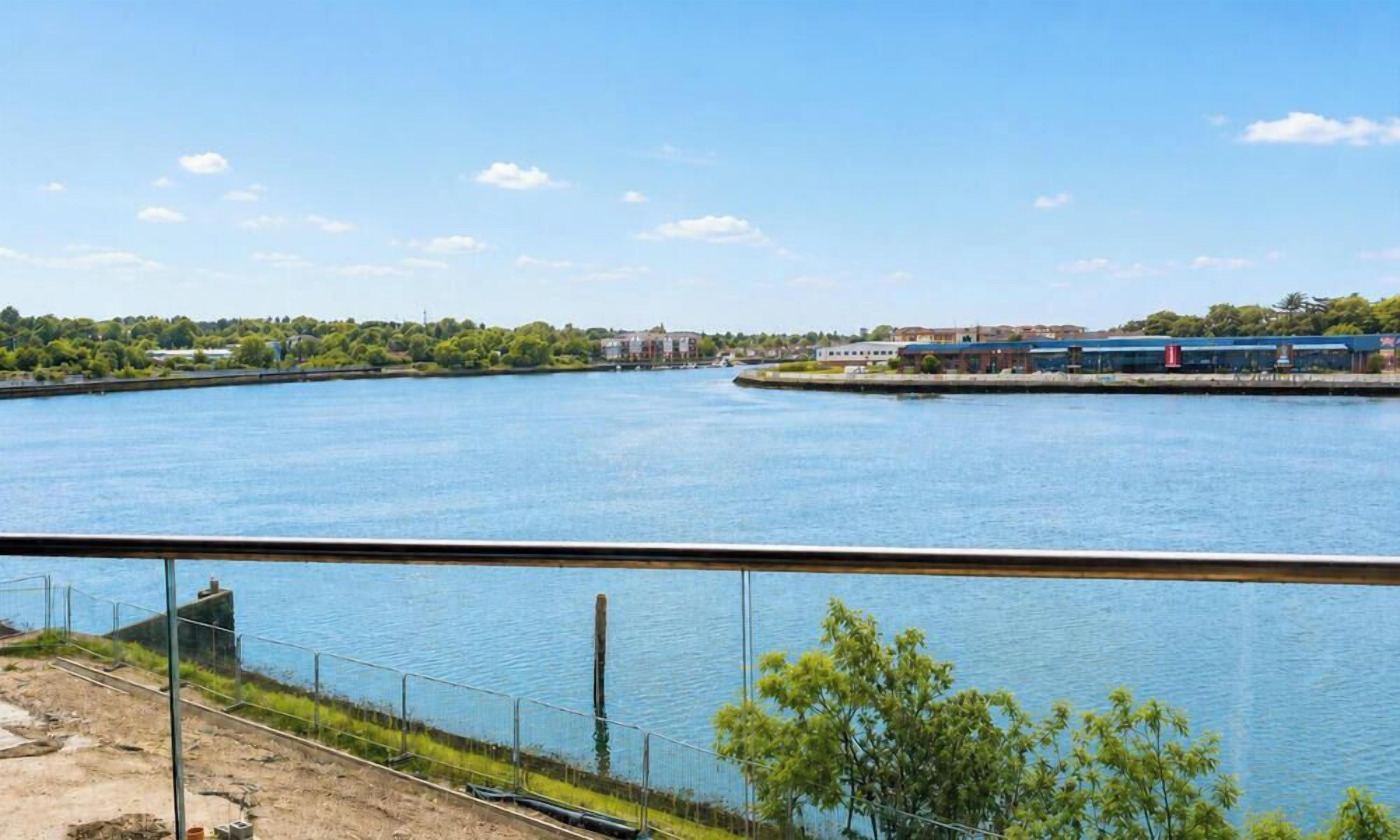 A waterfront view with a clear sky, a body of water, and a distant building complex.