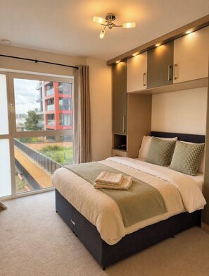 Ein Schlafzimmer mit einem großen Bett, einem Deckenventilator und Blick auf ein Gebäude durch eine Schiebetür.