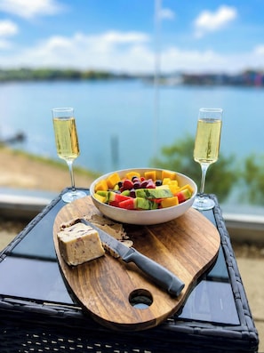 Ein Holzboden mit Obstsalat, zwei Gläsern Weißwein und einem Messer auf einem Tisch mit Blick auf ein Gewässer.