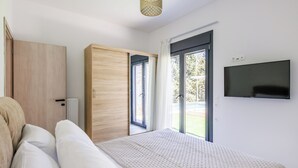 A bedroom with a bed, a wardrobe, a television, and a sliding glass door leading to an outdoor area. - Villa Theofilos-Country pool villa-3 bedrooms-wifi-sunset & sea view (Loutraki)