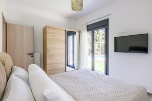 A bedroom with a bed, a wardrobe, a television, and a sliding glass door leading to an outdoor area. - Villa Theofilos-Country pool villa-3 bedrooms-wifi-sunset & sea view (Loutraki)