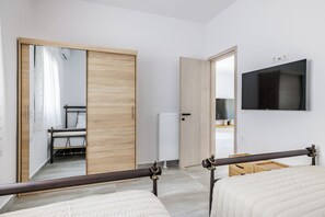Une chambre avec deux lits, une armoire en bois, un radiateur et un téléviseur fixé au mur.