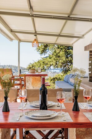 Un espace de restauration en plein air avec une table dressée pour deux personnes, une bouteille de vin et deux verres de vin rouge.
