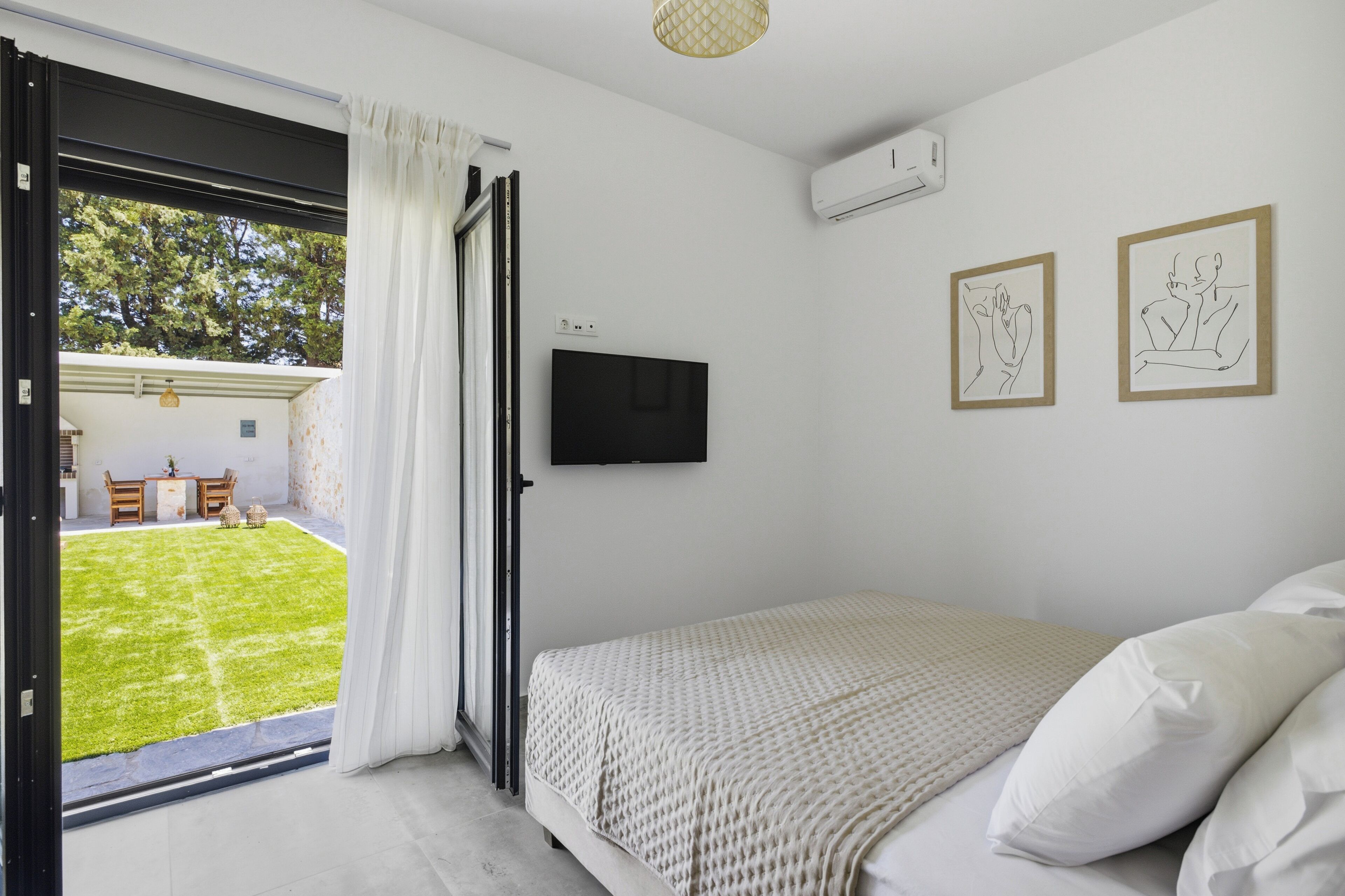A bedroom with a bed, a TV mounted on the wall, and two framed artworks.