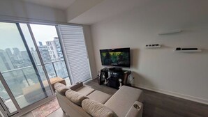 Un saló modern amb un sofà gran, una televisió de pantalla plana i una vista a la ciutat a través d'una porta corredissa de vidre.