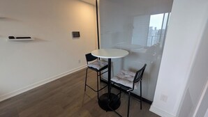 Habitació petita i moderna amb una taula rodona i dues cadires, una porta corredissa de vidre i vista a edificis a l'exterior.