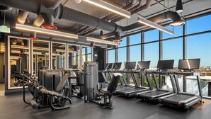 Ein Fitnessstudio mit Laufbändern, Krafttrainingsgeräten und großen Fenstern.