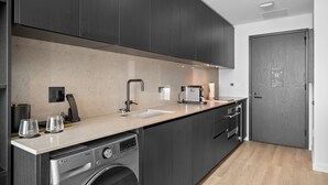 Eine moderne Küche mit dunklen Schränken, einem eingebauten Geschirrspüler und einer Arbeitsplatte mit Spüle und Kaffeemaschine.