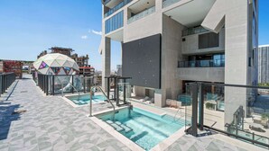 Ein Dachpool mit Glasgeländern, einer geometrischen Kuppelstruktur und einem modernen Gebäude mit Balkonen.