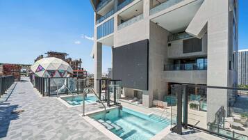 A rooftop swimming pool with glass railings, a geometric dome structure, and a modern building with balconies.