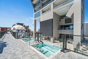 Ein Dachpool mit Glasgeländern, einer geometrischen Kuppelstruktur und einem modernen Gebäude mit Balkonen.