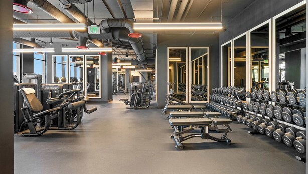 Ein Fitnessstudio mit Trainingsgeräten, Gewichtsständern und einem großen Spiegel.