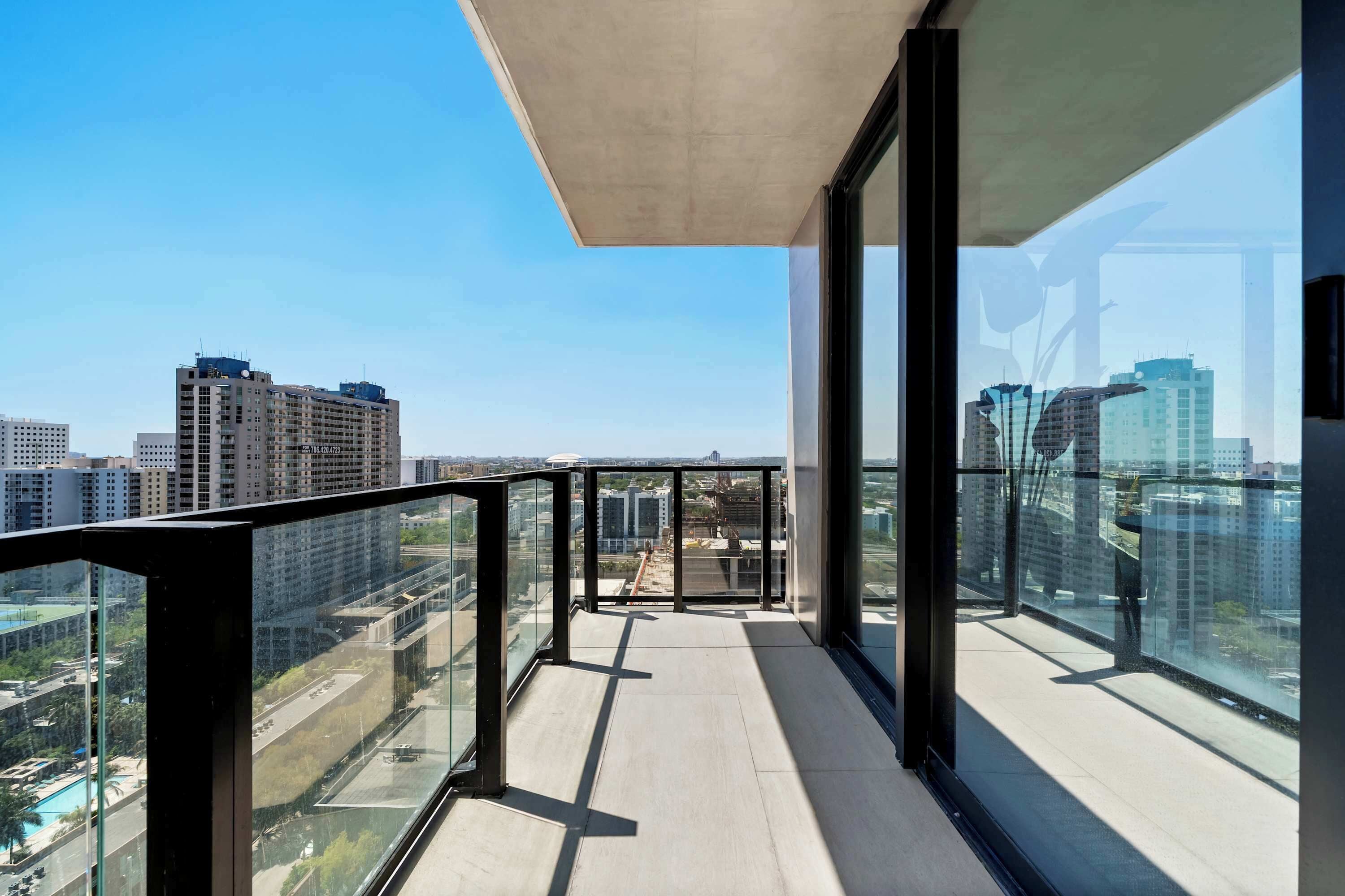 A modern balcony with glass railings, a concrete ceiling, and a city view.