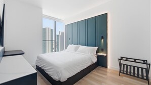 A modern bedroom with a bed, bedside table, and a view of the cityscape. - Luxury Condo w/ Rooftop Pool & City Views (Miami)