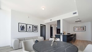 A modern living room with a round marble table, a grey sofa, and a bar area with stools. - Luxury Condo w/ Rooftop Pool & City Views (Miami)