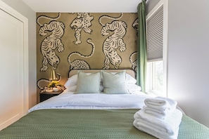 A hotel room with a bed, pillows, a nightstand with a lamp, and a wall with a leopard print design. - Luxury Boutique Stay w/ Hot Tub | Sleeps 8 | Near Golf Courses (Edmonton)