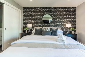 A hotel room with a large bed, a stone-patterned headboard, two bedside tables with lamps, and a mirror. - Luxury Boutique Stay w/ Hot Tub | Sleeps 8 | Near Golf Courses (Edmonton)