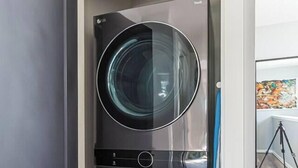 Ein kompakter, moderner Waschraum mit integrierter Waschmaschine und Trockner, einer kleinen Ablagefläche und einem Stativ im Hintergrund.