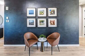 Ein modernes Interieur mit dunkler Wand, sechs gerahmten Bildern, zwei Ledersesseln und einem kleinen Tisch mit Pflanze.