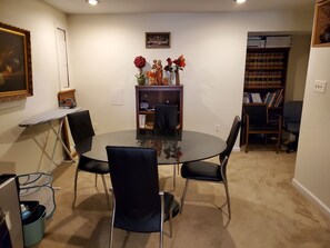 A room with a round glass table, four chairs, a bookshelf, a framed picture on the wall, and a small shelf with decorative items. - Delightful 2-bedroom Guest Suite with AC in Woodbridge (Woodbridge)
