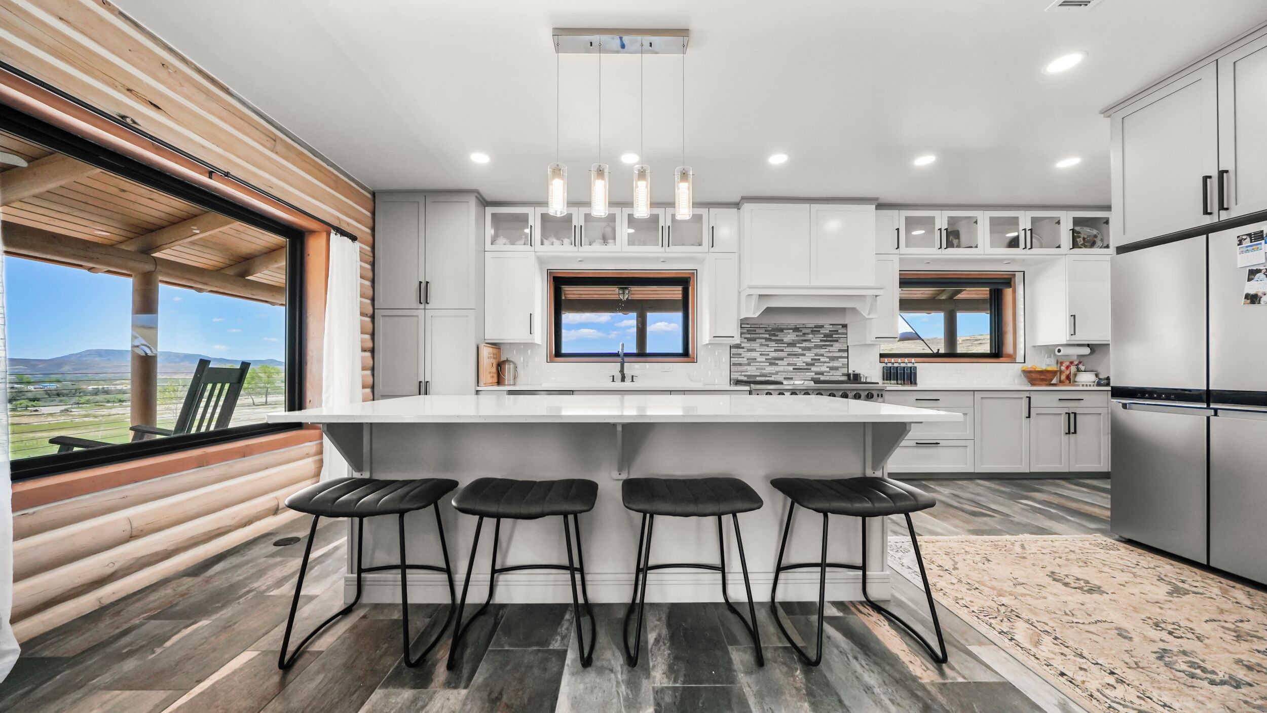 A modern kitchen with a central island, bar stools, and a view of the outdoors.