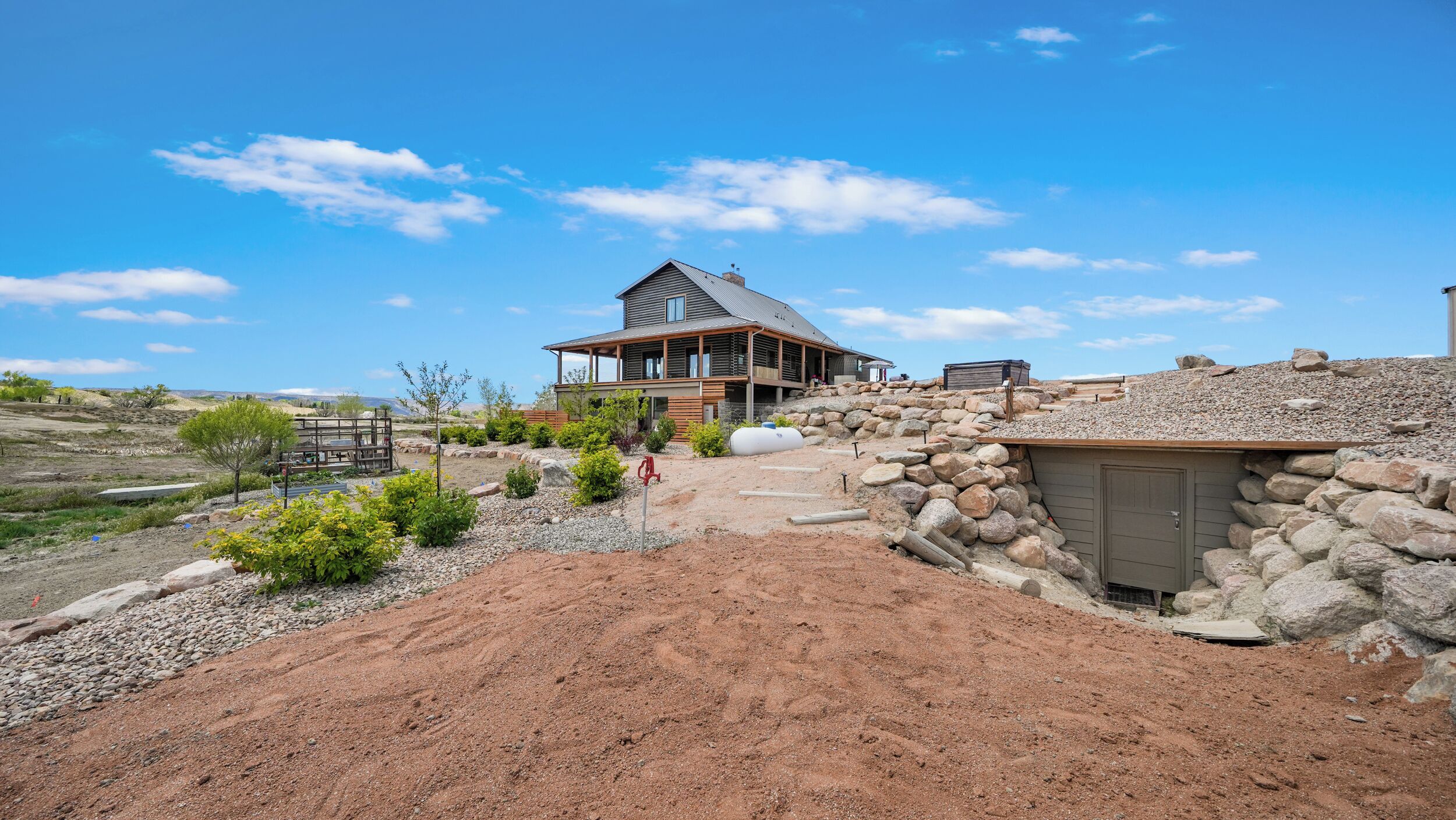 A modern house with a large porch, a stone retaining wall, and a gravel driveway.