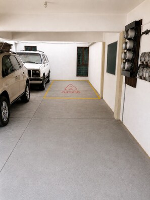 Un garaje para estacionamiento con dos autos estacionados, una puerta a la vista y un panel eléctrico en la pared.