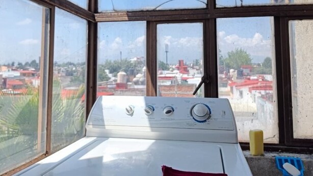 Una habitación con un ventanal grande, una lavadora y una toalla roja sobre la máquina.