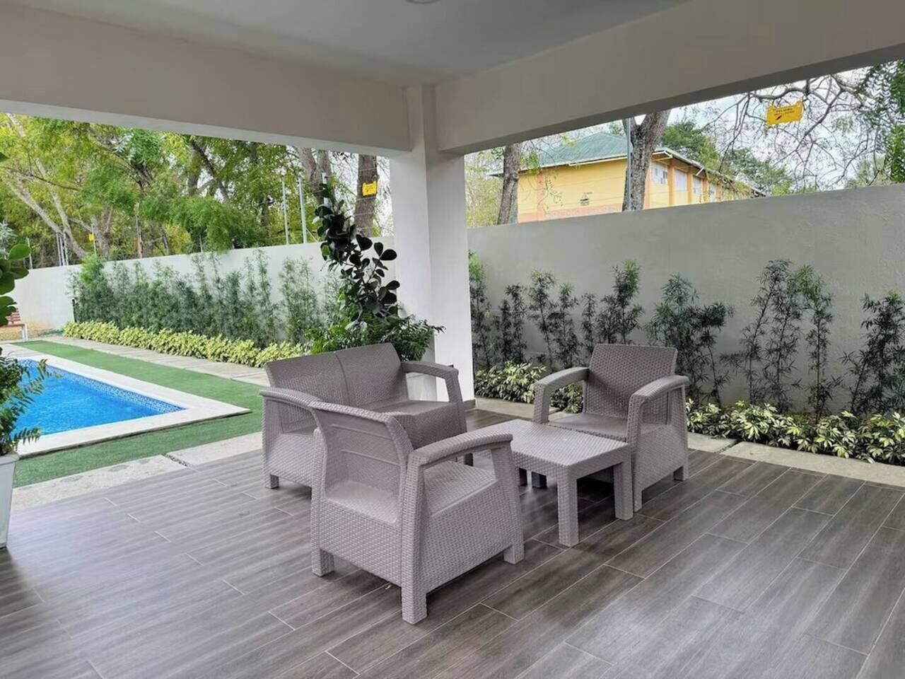 Un patio exterior con mobiliario de mimbre, una piscina y vistas a una zona residencial.