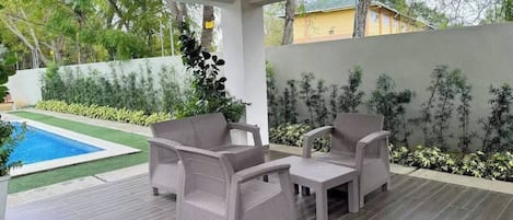An outdoor patio with wicker furniture, a swimming pool, and a view of a residential area.