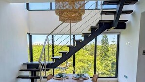 Et moderne spiseområde med et langt bord, stole og en trappe med gelænder i sort.