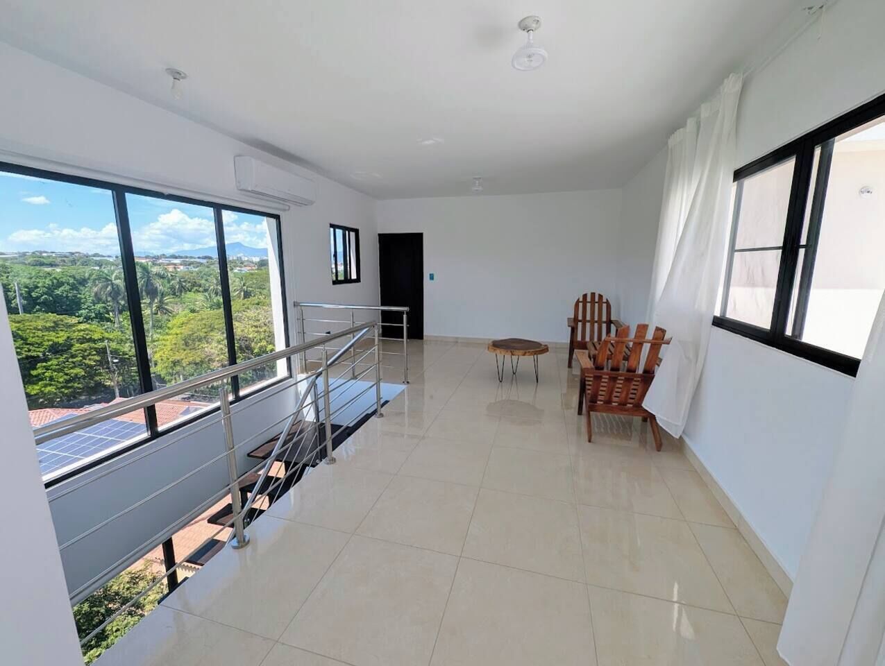 A spacious room with a balcony, a dining area with chairs, and a view of greenery outside.