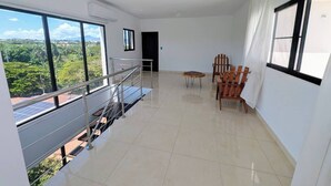 En rummelig stue med balkon, spiseplads med stole og udsigt til grønne omgivelser.