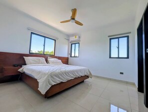 A bedroom with a bed, two windows, a ceiling fan, and an air conditioning unit.