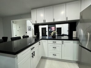 A modern kitchen with white cabinetry, black countertops, and a central island.