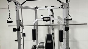 Et fitnessrum med en multifunktionel træningsstation, inklusiv en bænk, squatstativ og diverse vægtskiver.