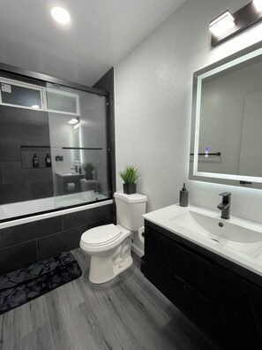 A modern bathroom with a bathtub, toilet, sink, and a large mirror. - Modern Spacious 4-bedroom house with AC in quaint Spring Valley (Spring Valley)