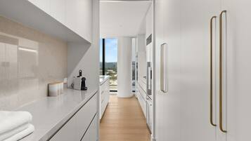 A modern kitchen with white cabinetry, a wooden countertop, and a view through an open door.