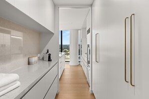 A modern kitchen with white cabinetry, a wooden countertop, and a view through an open door. - Altura Bay Luxury Residence Frankston (Frankston)