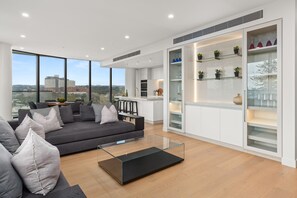 Una sala de estar moderna con un sofá gris, una mesa de centro de vidrio y vistas de la ciudad a través de amplias ventanas.