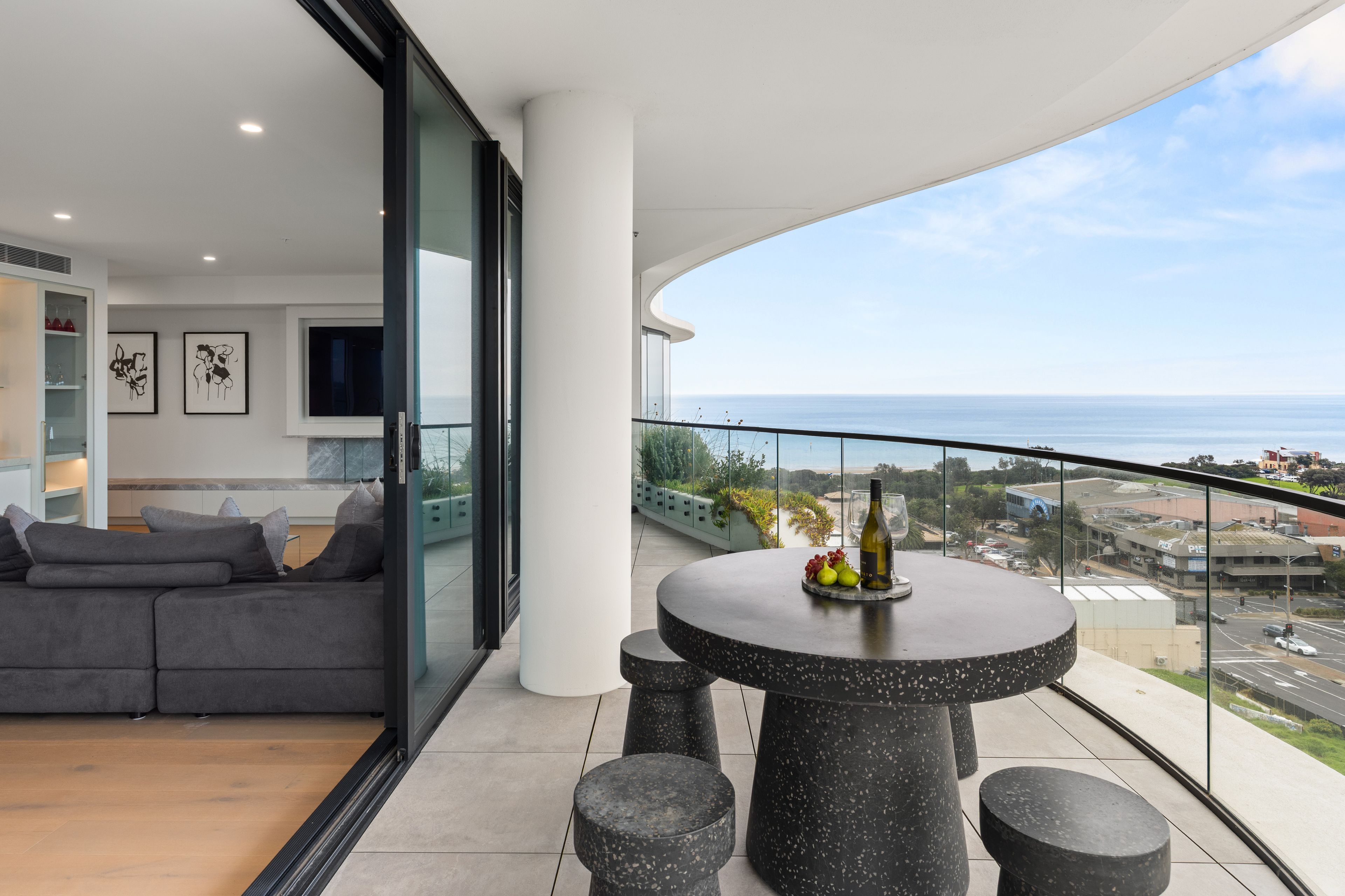 A modern balcony with a round table, seating, and a view of the sea.