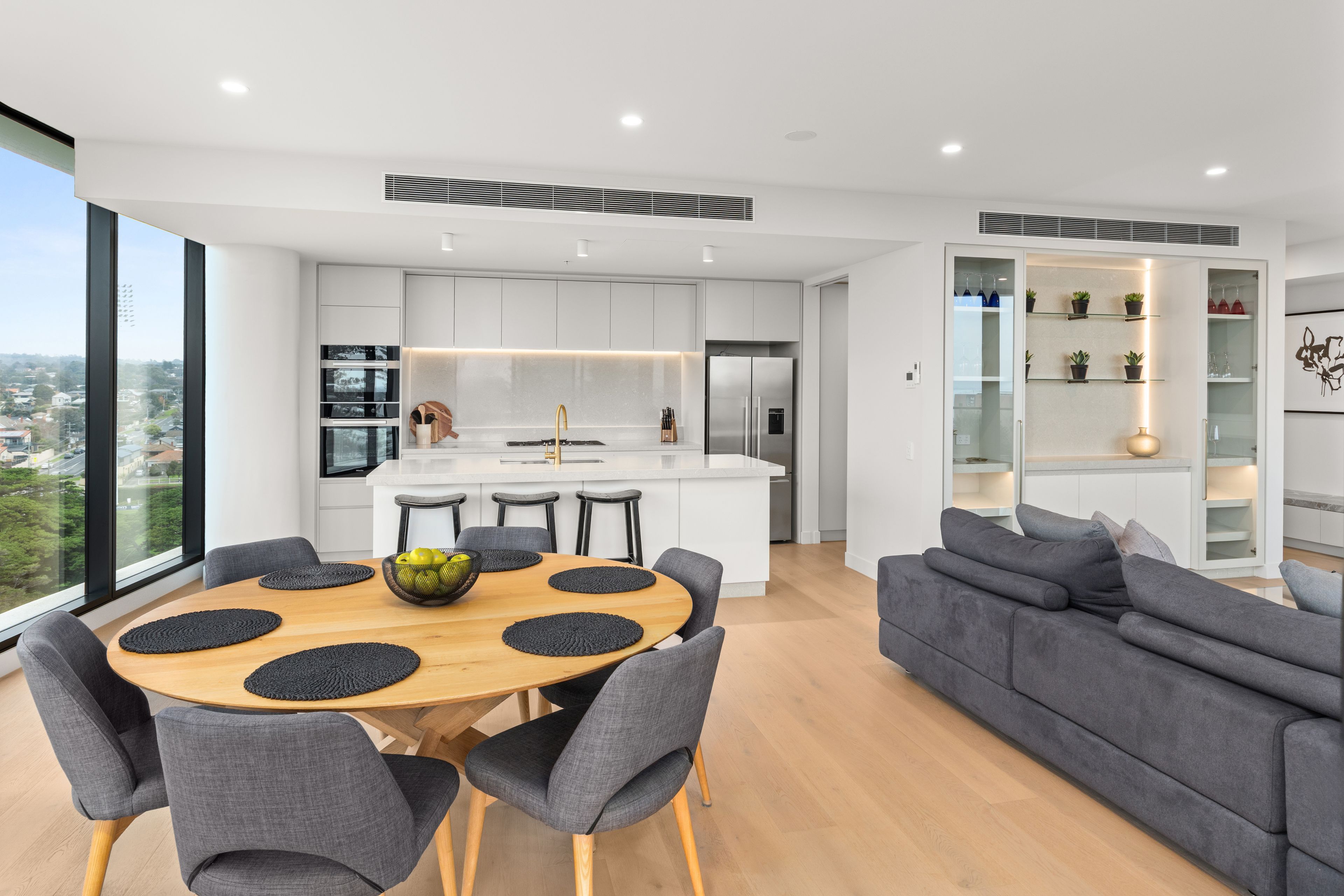 A modern kitchen with white cabinets, a central island, and a dining area with a wooden table and grey upholstered chairs.