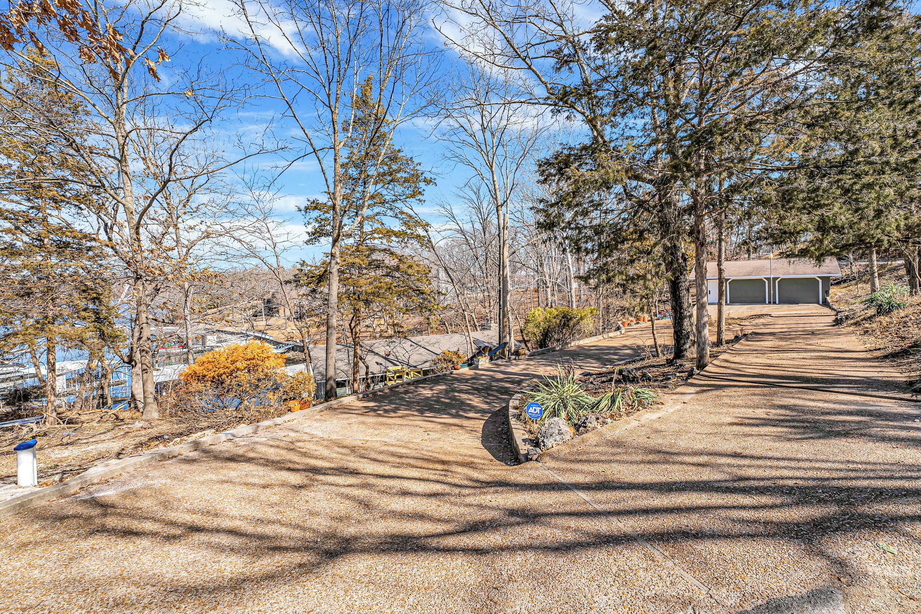 A paved pathway leading to a building with a garage, surrounded by trees and a clear sky.