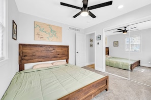 Une chambre à coucher avec une tête de lit en bois, une couvre-lit verte, un ventilateur de plafond, une carte accrochée au mur et un grand miroir qui reflète la pièce.