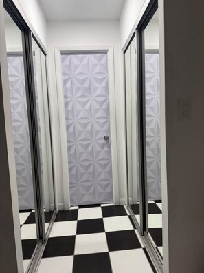 Ein Flur mit Schachbrettfußboden, einer geometrisch gemusterten Tür und gespiegelten Wänden.