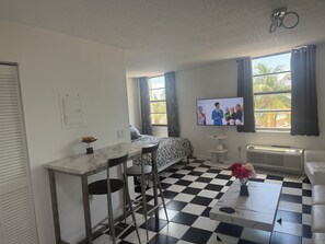 Um quarto com cama, escrivaninha, cadeiras, televisão e radiador.